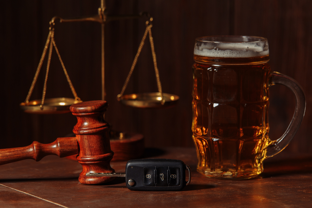 Beer mug, car keys, and a gavel placed near scales of justice illustrating DUI evidence and law.