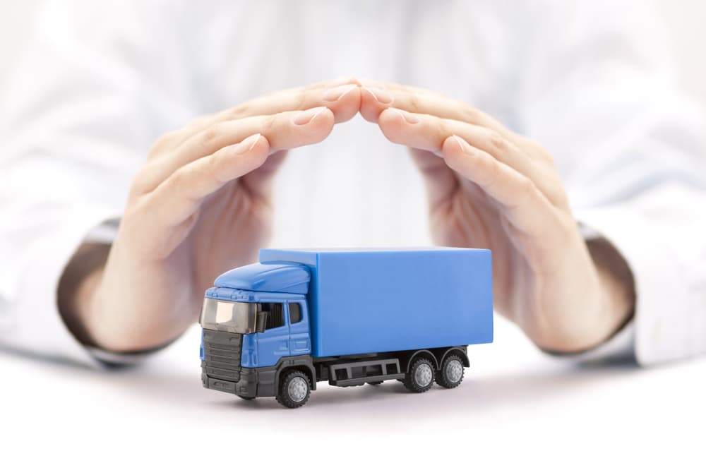 Hands protecting a miniature blue truck symbolizing insurance coverage for trucks.