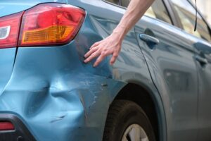 Person inspecting rear end dent and paint damage on a blue car after a hit and run accident in Missouri representing vehicle damage in a car accident claim