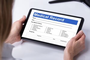 Close-up of a female doctor reviewing a patient's information form on a digital tablet over her desk. 