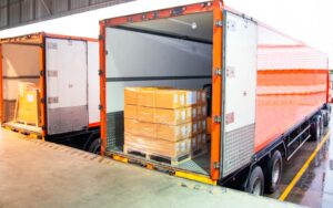 A cargo freight truck engaged in shipment and delivery services, part of logistics and transportation, loading pallet goods at a warehouse dock into a shipping container truck.