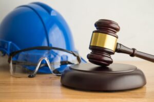 A judge's gavel and a construction hat, along with worker safety glasses, sit on a wooden background, symbolizing labor law concepts such as wages, overtime pay, and worker welfare. 