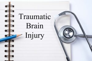 A stethoscope rests on a notebook with the words "traumatic brain injury," accompanied by a pencil, representing a medical concept. 