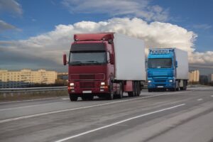 Trucks delivering cargo on the highway with a cityscape in the background.