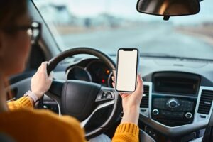 Woman driver using mobile phone screen blank mockup while driving distracted from the road