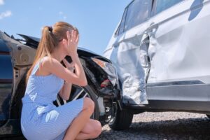 Sad female driver sitting on street side shocked after car accident