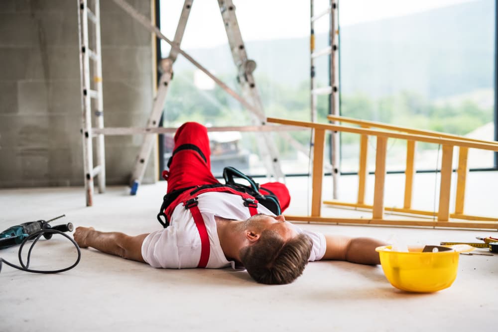 A male worker is lying on the ground following an accident at a construction site.