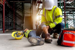 First aid support is crucial following an accident at a construction site. In this scenario, a construction worker falls from scaffolding and lies injured on the floor.