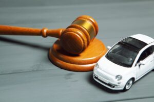 A car and a hammer are placed on a table, symbolizing the intersection of automobiles and legal action, possibly representing car accident or a lawsuit.