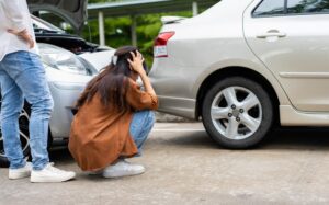 An Asian woman inspects her car for damage after an accident before taking photos and submitting an online insurance claim.