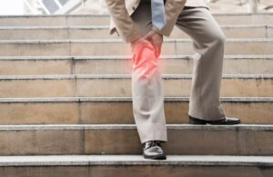 A businessman sitting on a staircase, suffering from knee pain. 