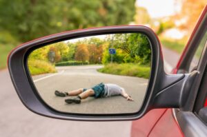 A rearview mirror reflects the scene of a car accident, showing a man who has been struck by a vehicle, emphasizing the concept of traffic collisions.