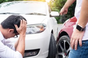 Two men are arguing intensely on the road after a traffic collision, with their damaged cars in the background.