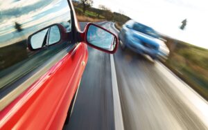 A man drives a red car directly towards an oncoming vehicle.