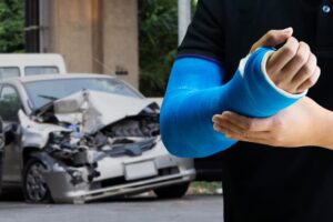 Close-up of a man holding his arm with a blue bandage, indicating an arm injury from a car accident.