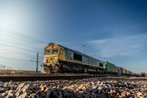 Profile view of a goods train with intermodal wagons loaded with shipping containers for import and export, positioned in a yard or sidings