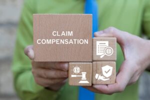 Man holding wooden blocks with icons and text displaying 'CLAIM COMPENSATION' as part of a business finance concept, with a registration claim document in the background.