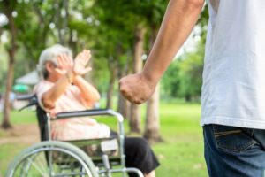 Asian elderly woman in a wheelchair being physically abused by an angry man or caregiver raising a fist in an outdoor setting, illustrating the concept of stopping violence and aggression against senior people.