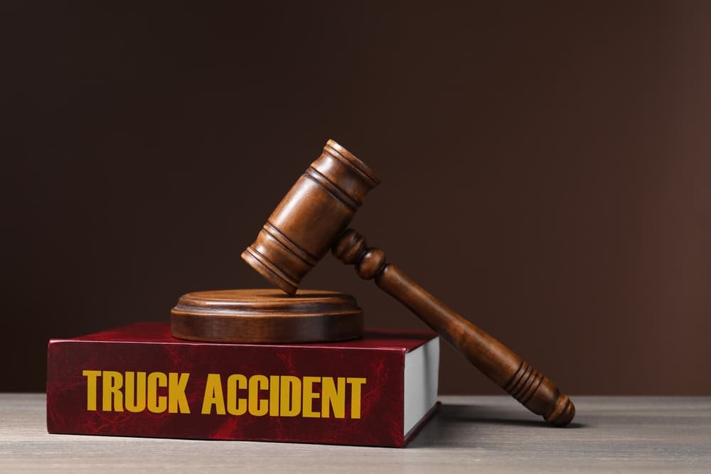 Truck accident law book and judge's gavel placed on a wooden table with a brown background.