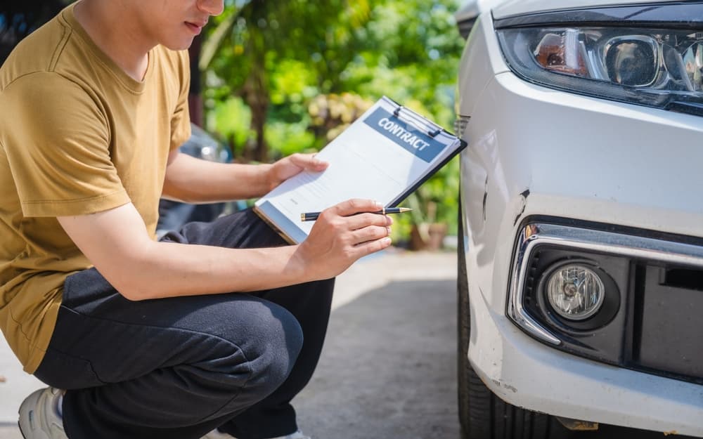 Man fills out a car insurance form after a car accident. Comprehensive motor insurance covers car damage.