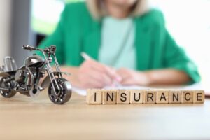 Motorcycle model and word insurance on table, blurred manager with documents in background.