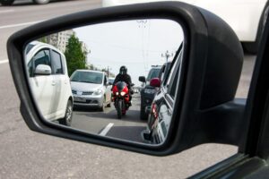A car driver watching in side mirror a motorcyclist passing