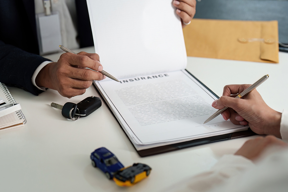 Client signing an insurance agreement while an agent reviews paperwork, representing a settlement release decision.