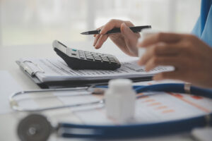 Doctor using a calculator and laptop with a stethoscope on the desk, representing medical costs after a car accident.