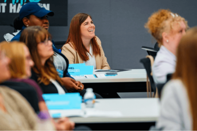 Rachael Leadbetter laughing during a Crisp Experience session, seated at a table with her name placard visible, surrounded by other attendees.