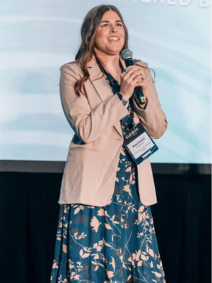 Rachael Leadbetter speaking on stage at the Crisp ELEVATE Conference in Orlando, Florida, holding a microphone and wearing her conference badge.
