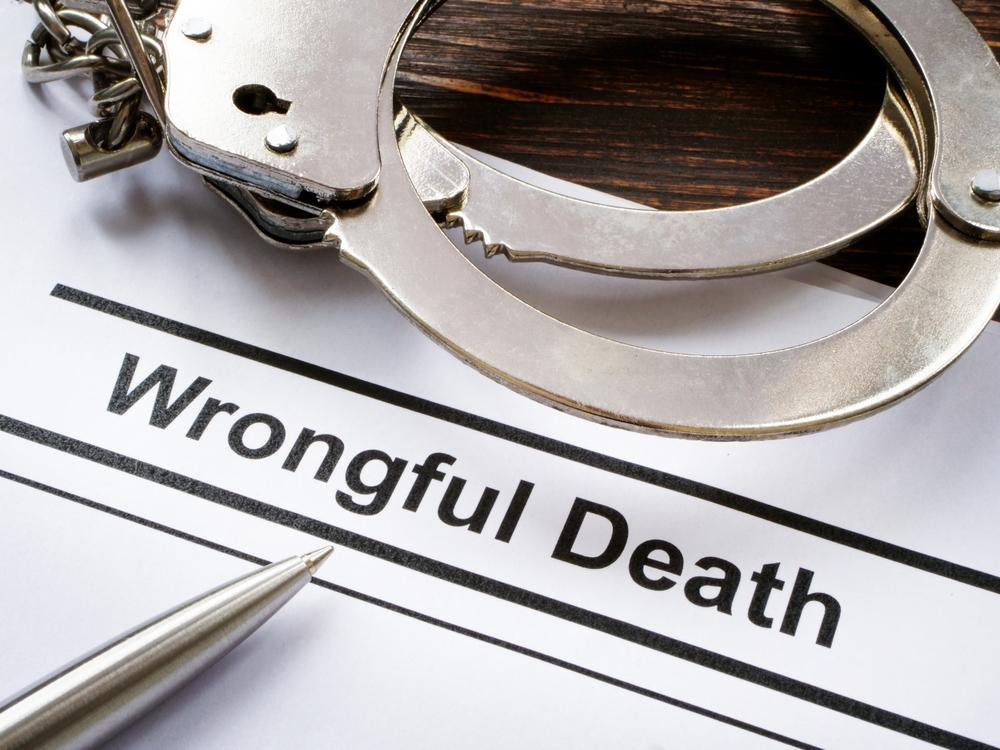 Document titled wrongful death beside a pair of handcuffs and a silver pen
