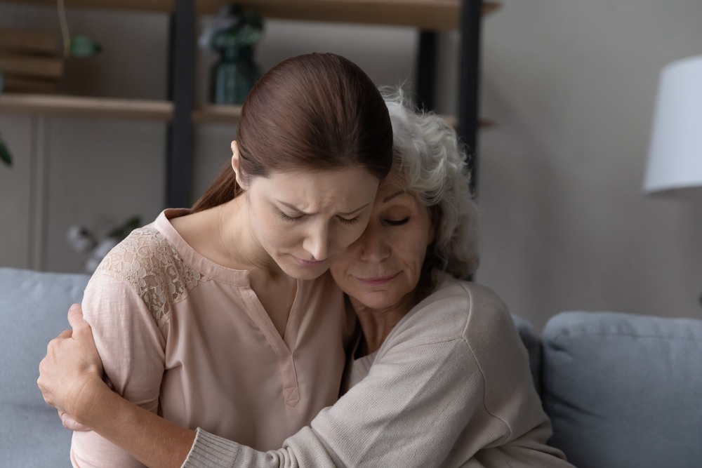 Grieving young woman and older woman holding each other on a couch at home